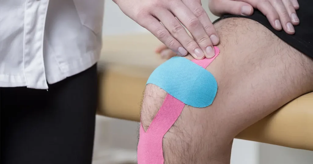 Kinesio taping a domicilio in Lombardia: un professionista della riabilitazione applica nastri neuromuscolari sul ginocchio di un paziente per favorire il recupero funzionale direttamente a casa.