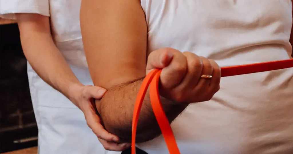 Riabilitazione cardio-respiratoria a domicilio in Lombardia: un professionista assiste il paziente in esercizi terapeutici con elastico per il miglioramento della funzionalità cardiaca e respiratoria direttamente a casa.