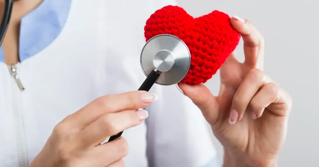 Visita cardiologica a domicilio in Lombardia: un medico specialista utilizza lo stetoscopio su un cuore simbolico per rappresentare la prevenzione e la cura cardiaca direttamente a casa.